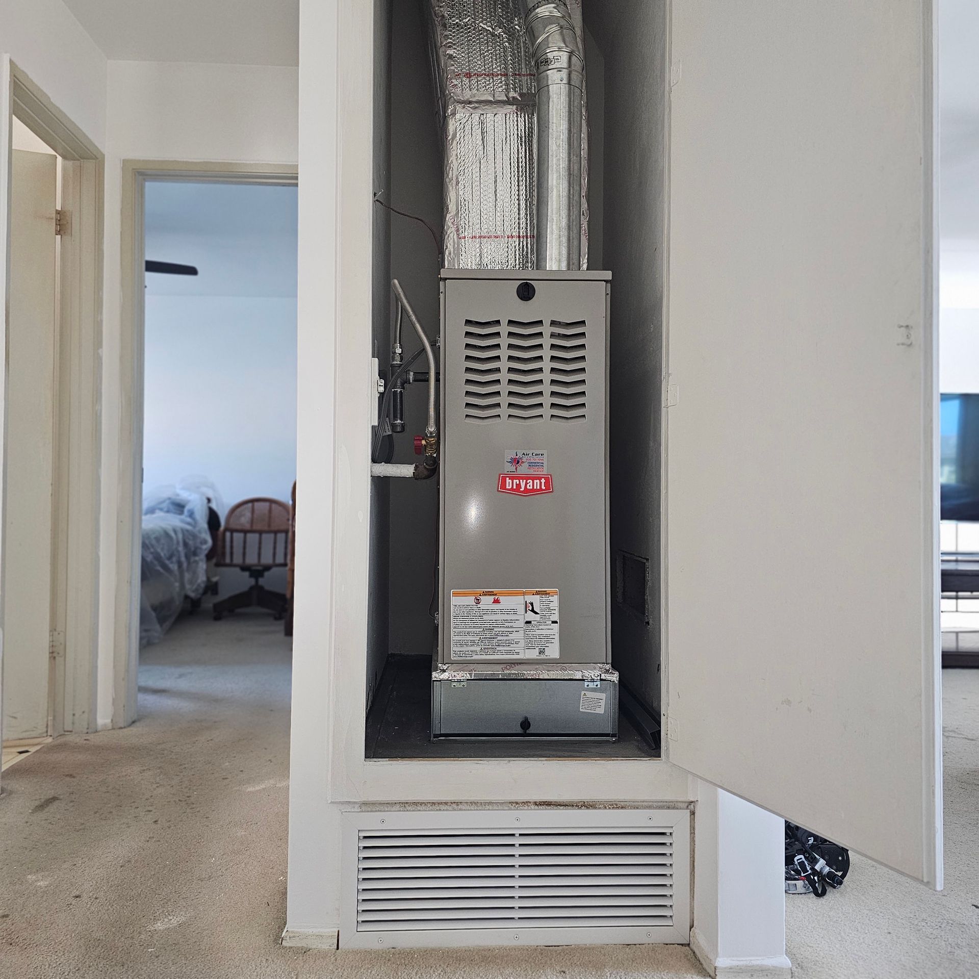 Open furnace in a hallway closet with white doors and vent grille.