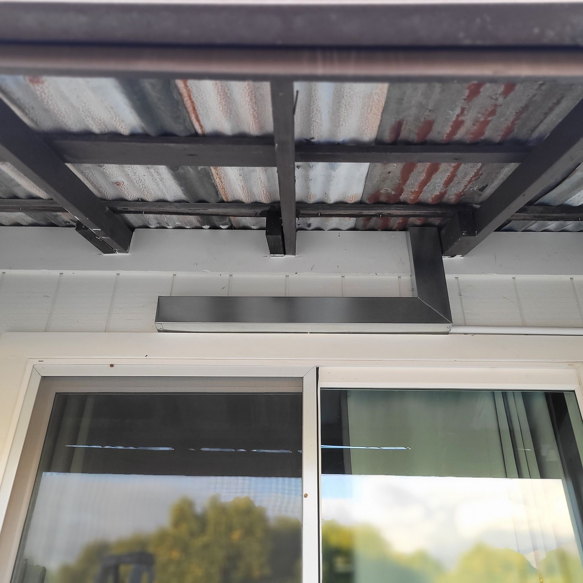 Underside of a corrugated metal awning above a sliding glass door on a white exterior wall