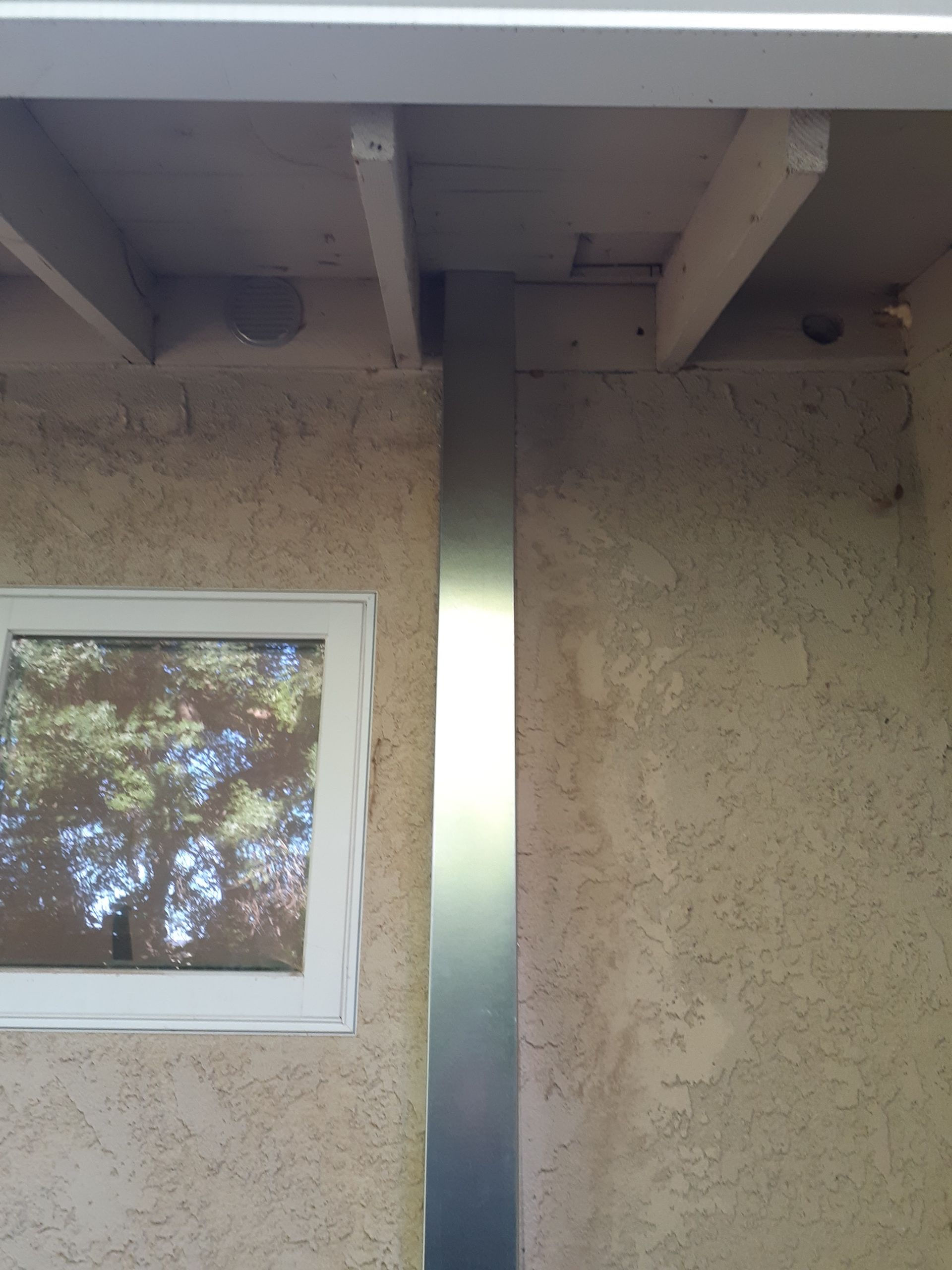 Stucco wall with a window, exposed ceiling beams, and a tall metal column outdoors
