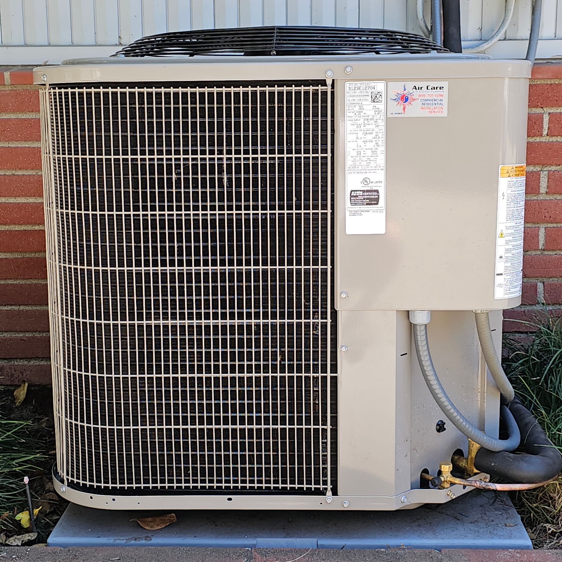 Outdoor beige HVAC condenser unit beside a house, with a large front grille and visible hoses.