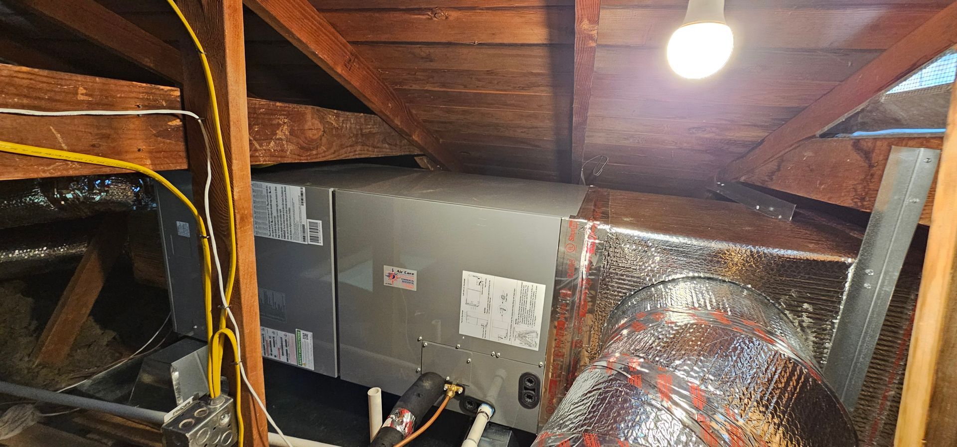 Attic crawl space with exposed insulation, ductwork, wiring, and a single hanging light bulb