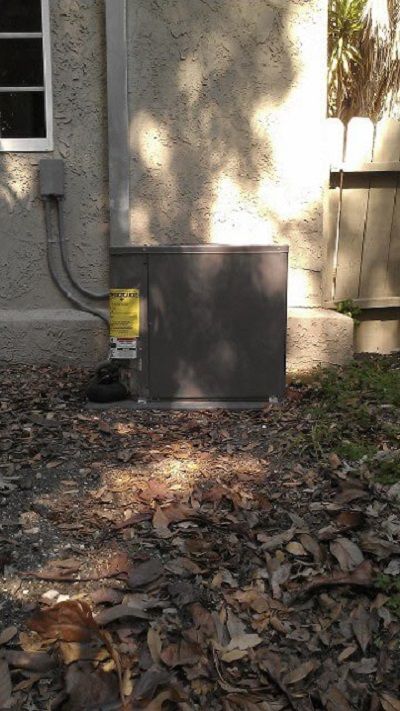 Yellow utility meter beside a stucco house wall, with dry leaves and a wooden fence in the yard.