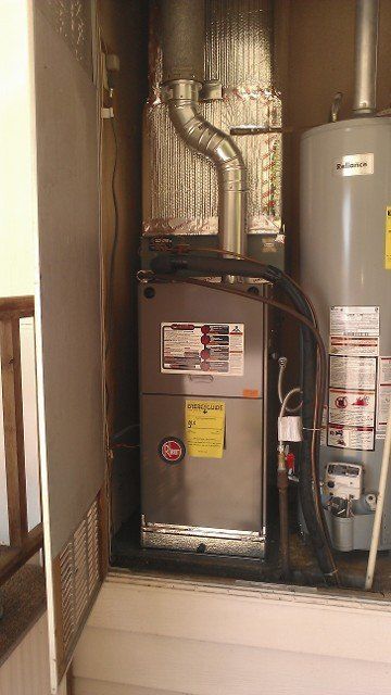 Utility closet with furnace, water heater, and exposed ductwork inside a small indoor space.