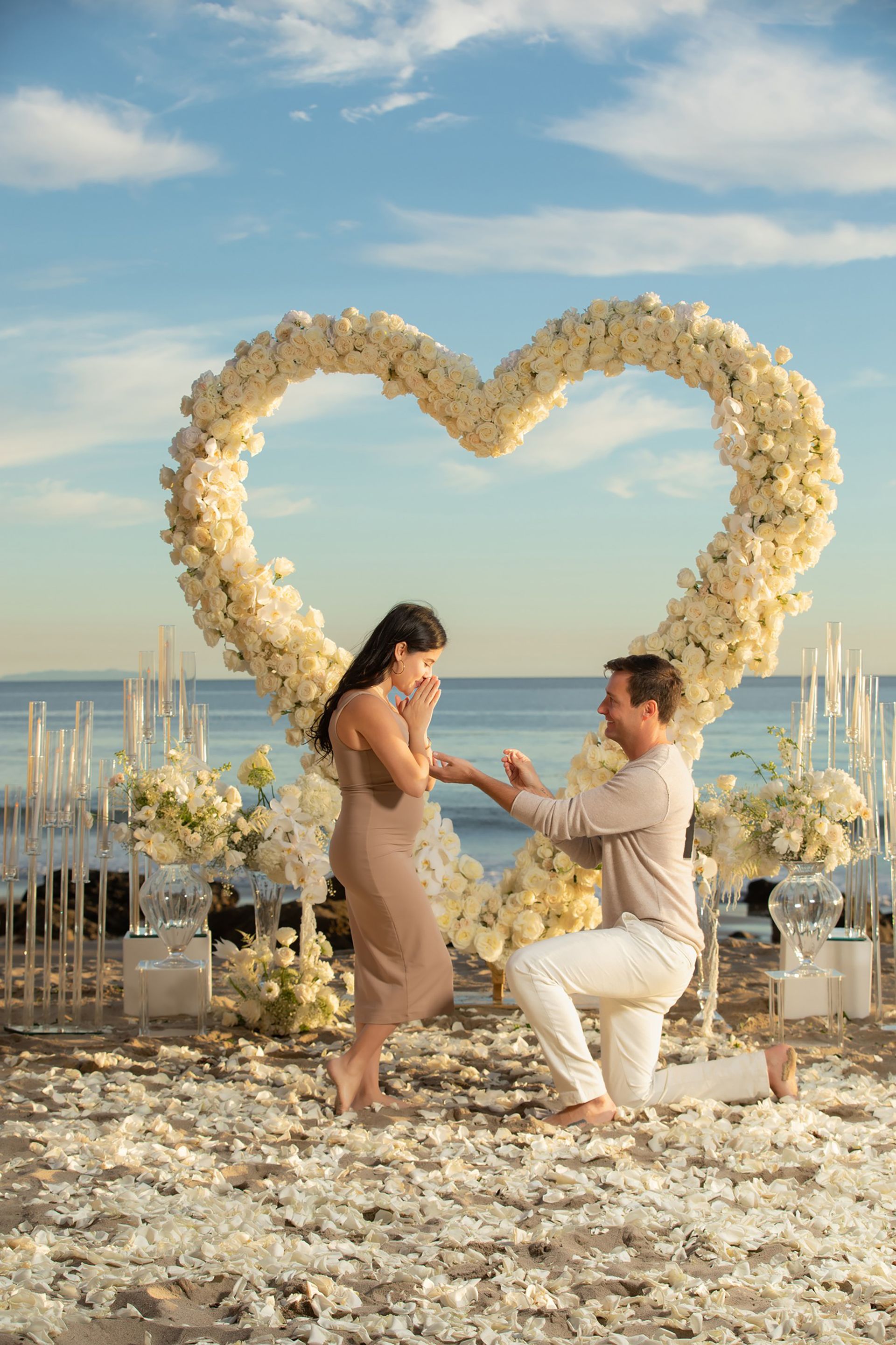 A couple embracing during a surprise sunset proposal at El Matador Beach, with dramatic cliffs and ocean waves in the background.
