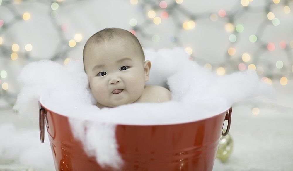 A baby is taking a bath in a red bucket filled with foam.