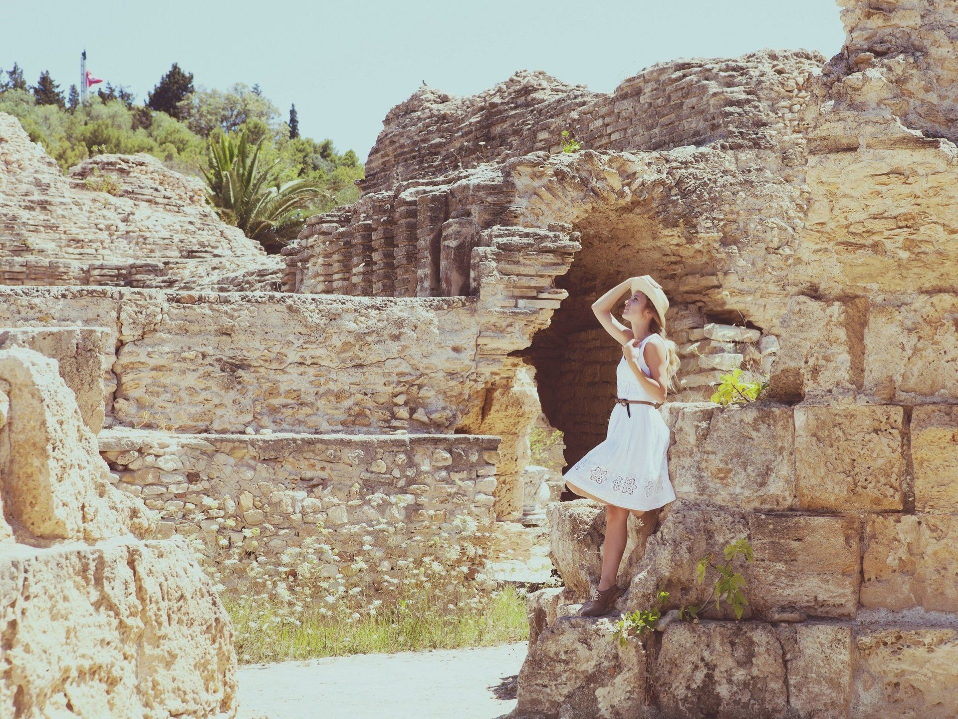A woman in a white dress and hat is standing on a stone wall.