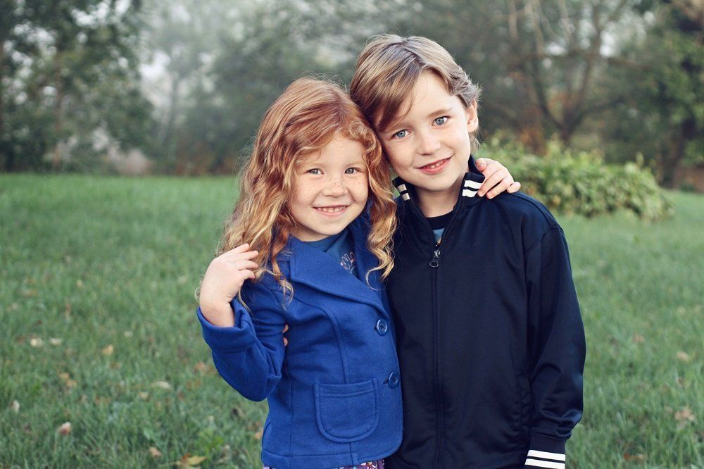 A boy and a girl are standing next to each other in a field.