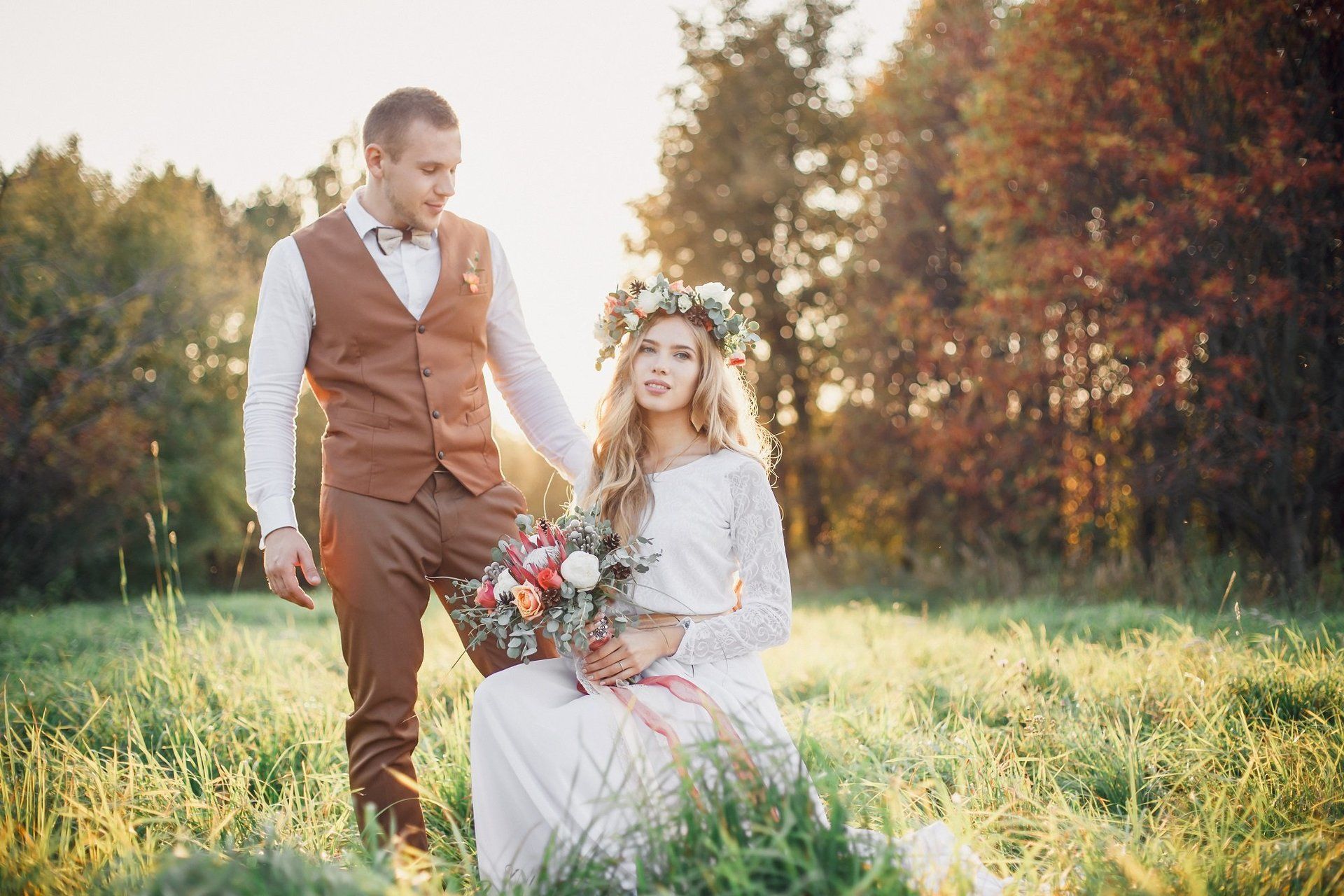 A bride and groom are standing in a field holding hands.