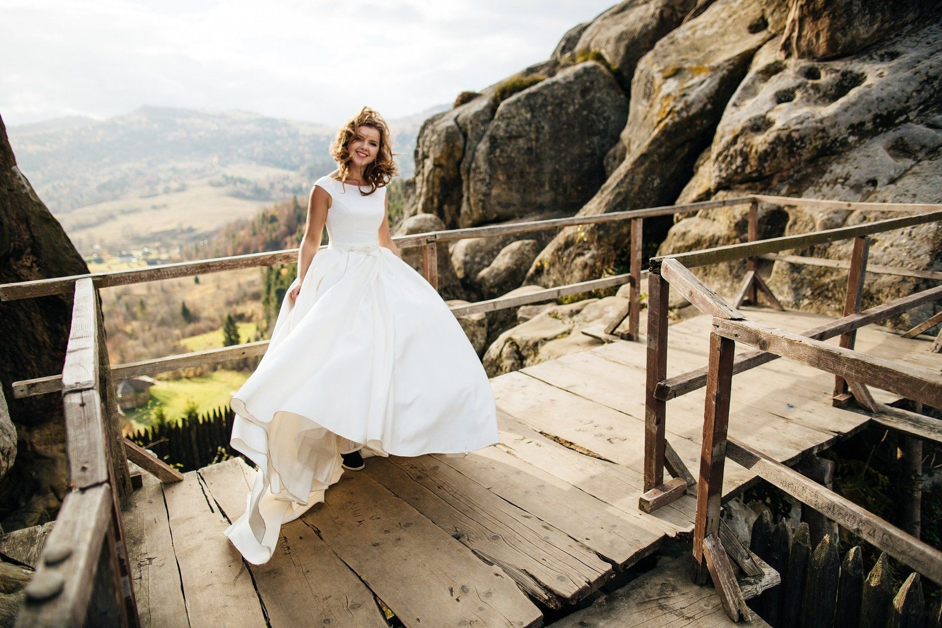 A woman in a wedding dress is standing on a wooden bridge.