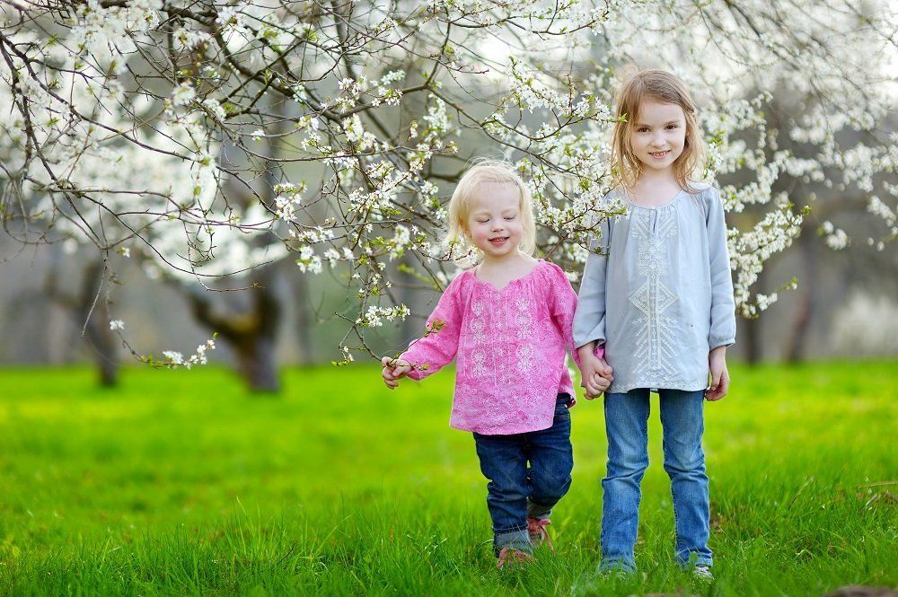 Two little girls are holding hands in a park.