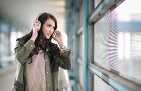 A woman is wearing headphones and looking out a window.