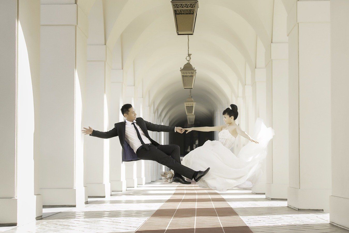 A bride and groom are flying through the air in a hallway.