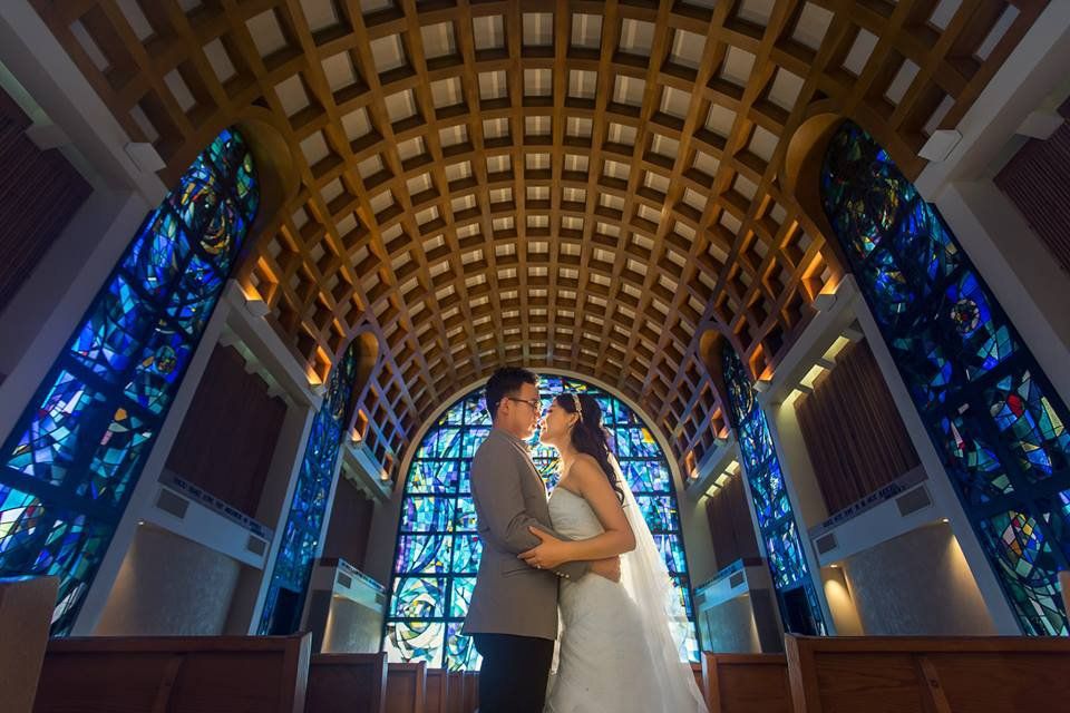 A bride and groom are kissing in front of a stained glass window in a church.