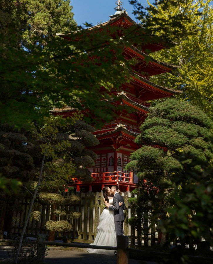 A bride and groom are kissing in front of a pagoda.