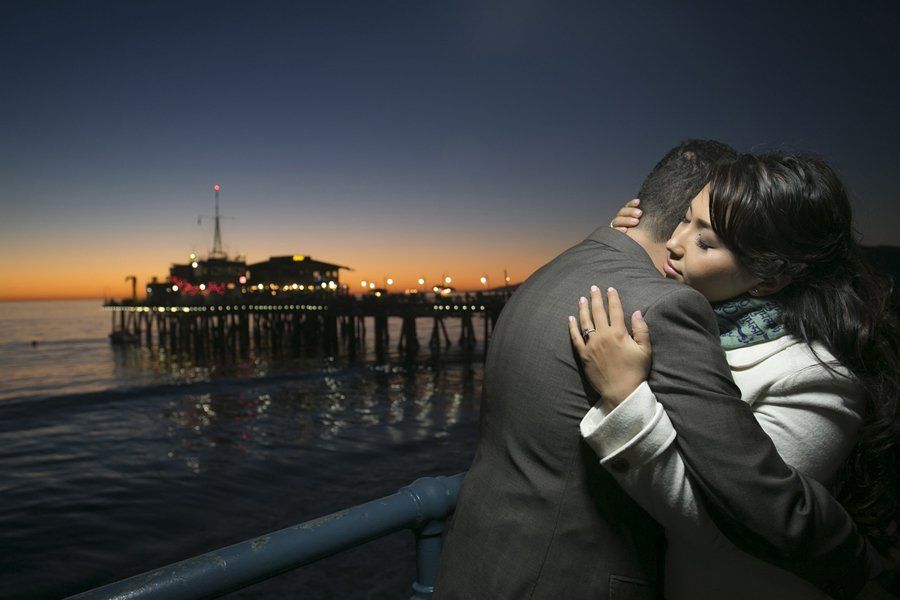 A man and a woman are hugging each other on a pier at sunset.