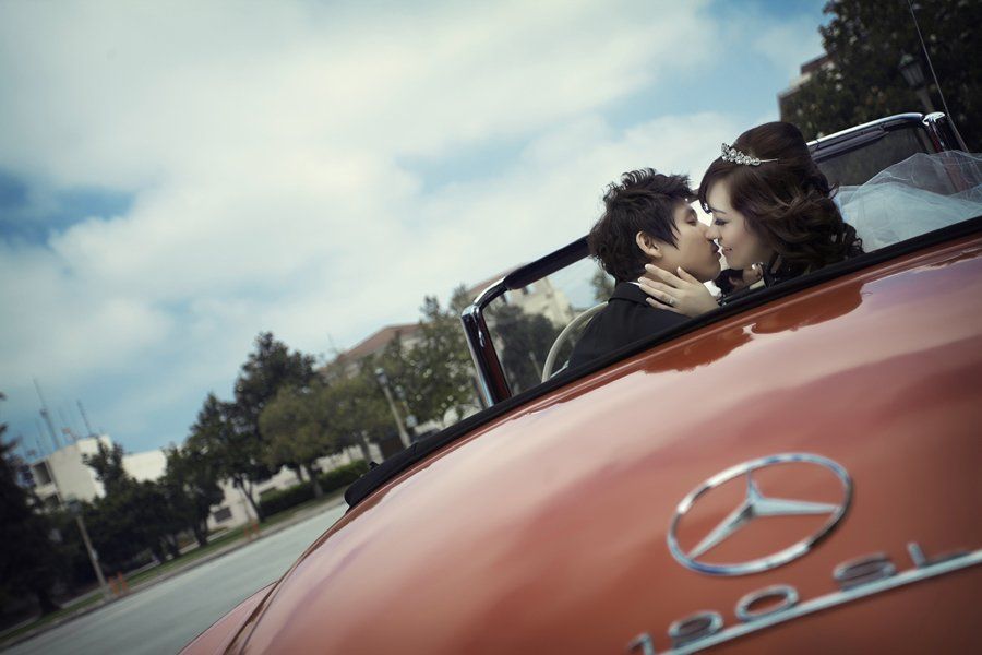 A bride and groom kissing in the back of a red mercedes