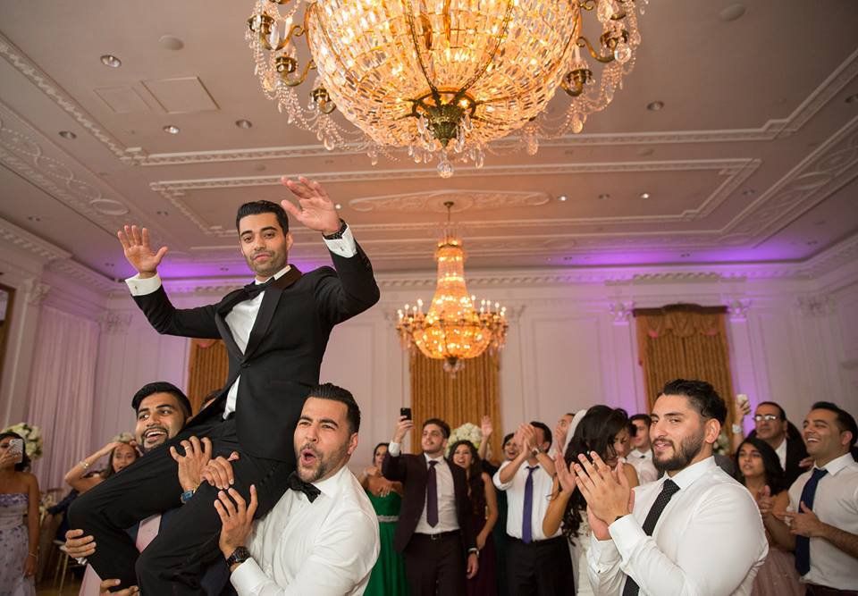 A man in a tuxedo is being lifted in the air by a group of people at a wedding reception.
