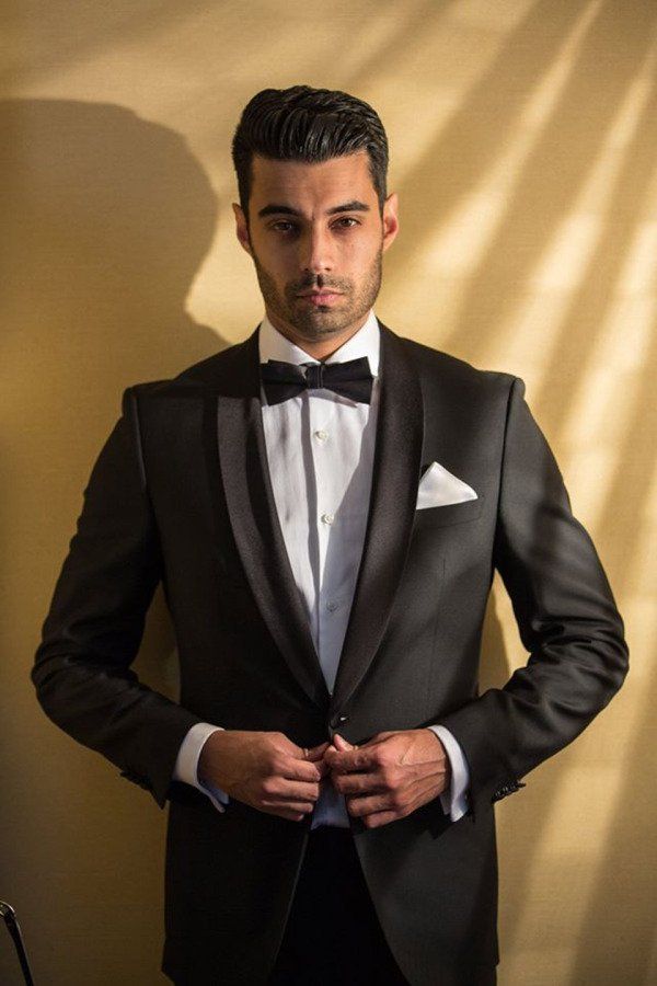 A man in a tuxedo and bow tie is adjusting his jacket.