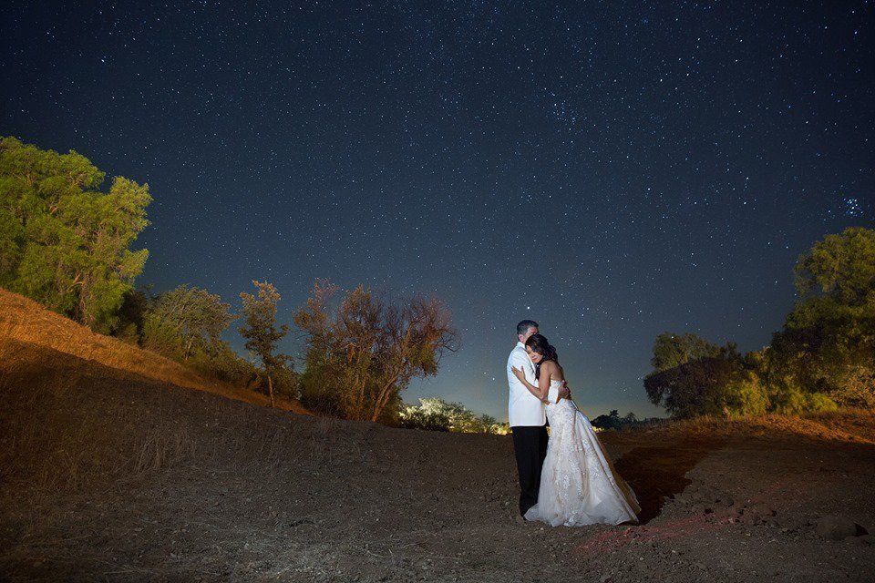 A bride and groom are kissing under a starry night sky.