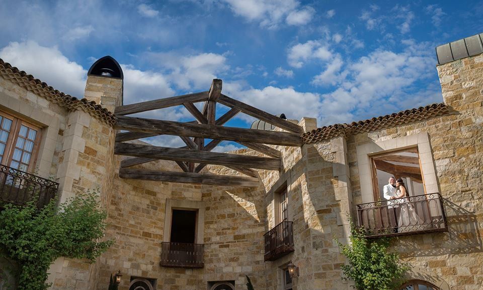 A bride and groom are standing on a balcony in front of a large stone building.