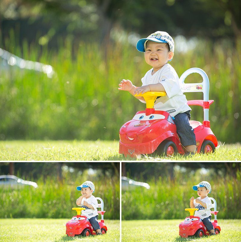A baby is sitting on a red toy car in the grass.