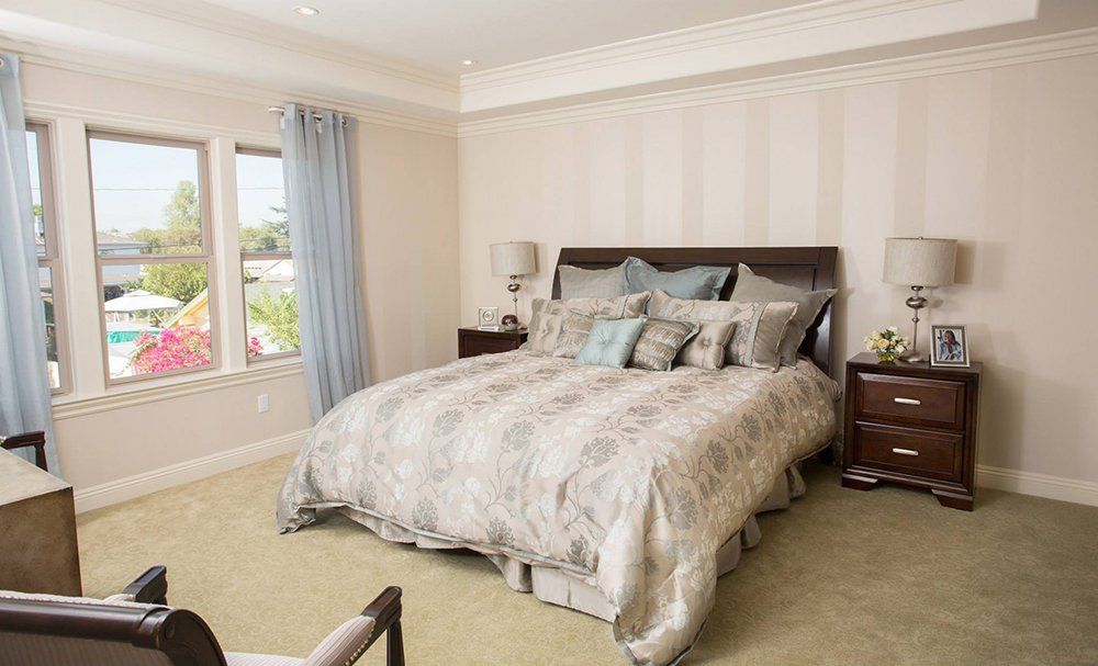 A bedroom with a large bed , two nightstands , a chair and two windows.