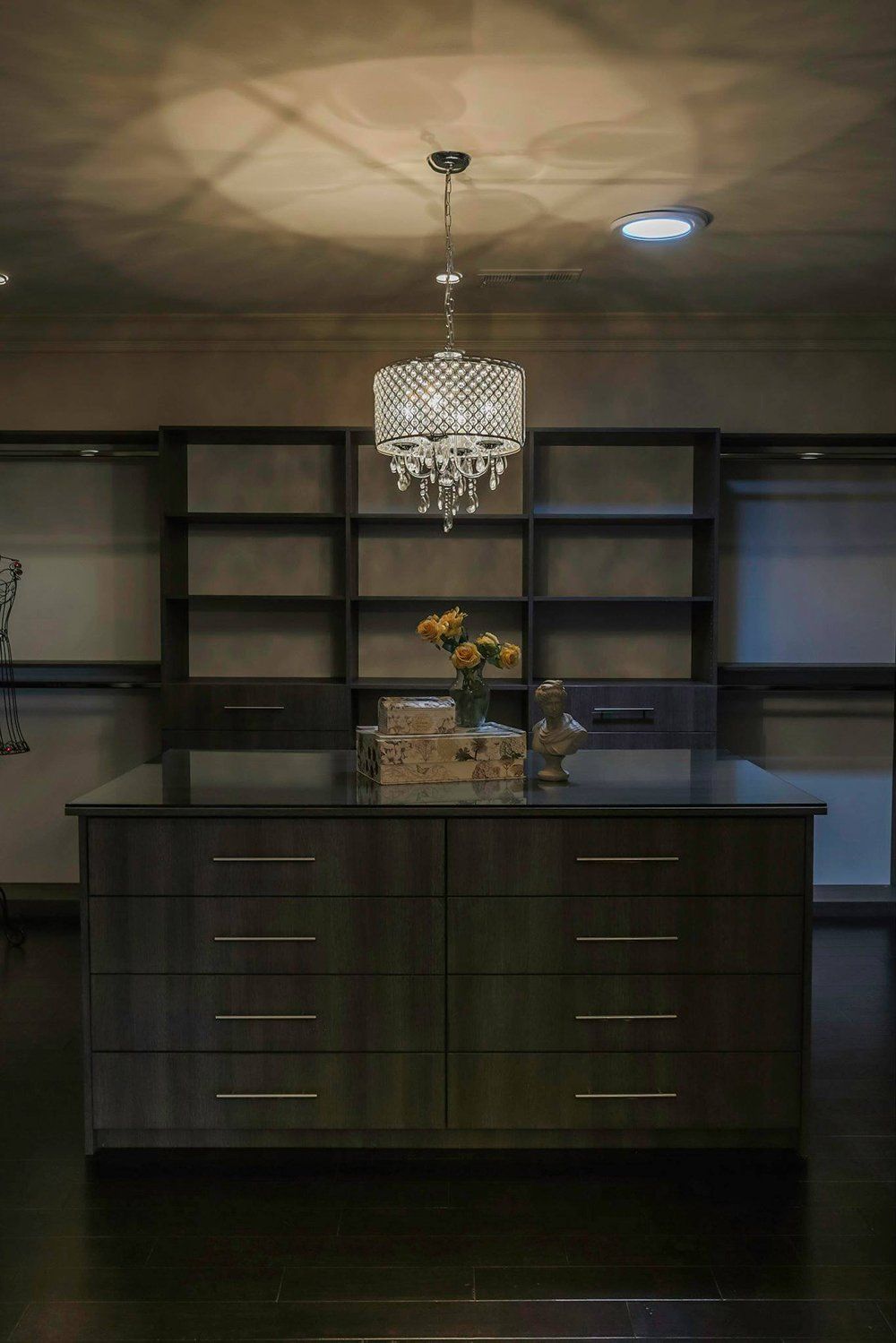 A walk in closet with a large island in the middle and a chandelier hanging from the ceiling.