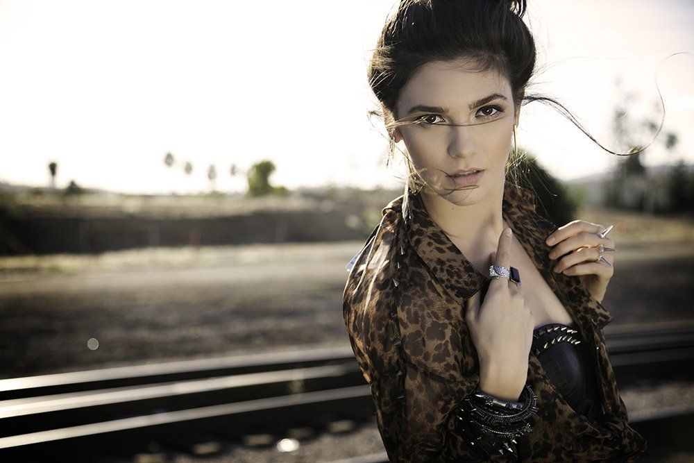 A woman in a leopard print shirt is standing on train tracks.