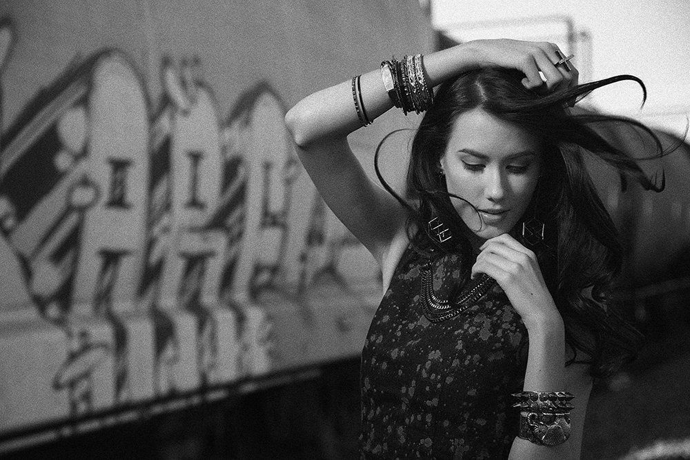 A black and white photo of a woman standing in front of a graffiti wall.