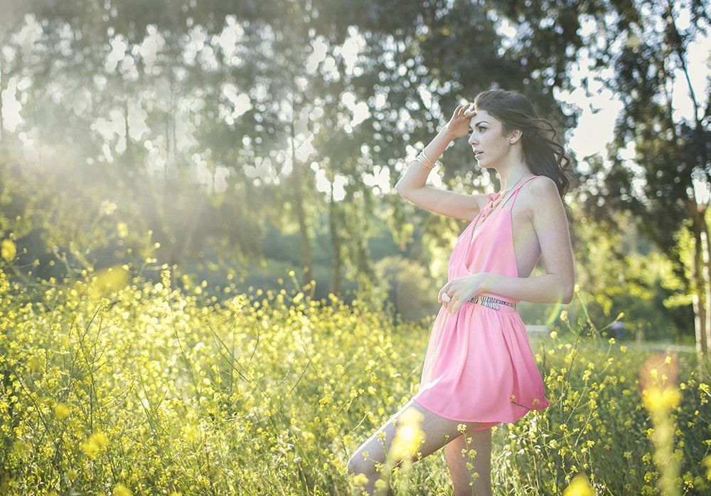 A woman in a pink dress is standing in a field of yellow flowers.