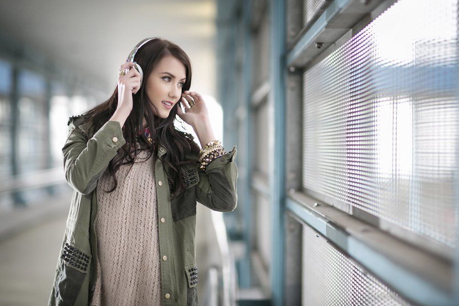 A woman is wearing headphones and looking out a window.