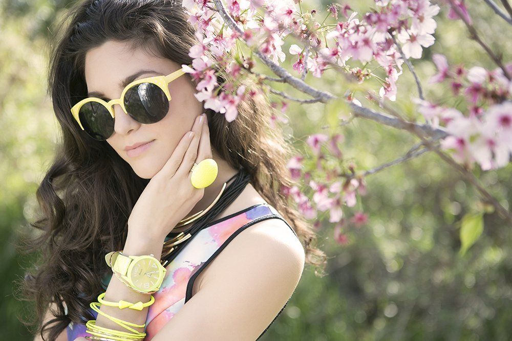 A woman wearing sunglasses and a watch is standing in front of a tree with pink flowers.