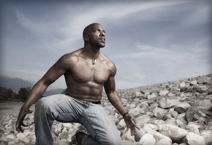 A shirtless man is squatting on a pile of rocks