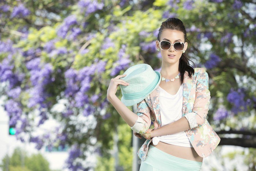 A woman wearing sunglasses and a hat is standing in front of a tree.
