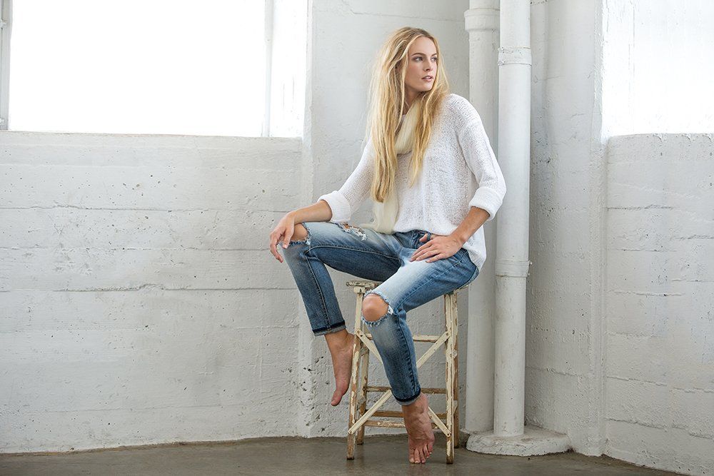 A woman is sitting on a wooden stool in a room.