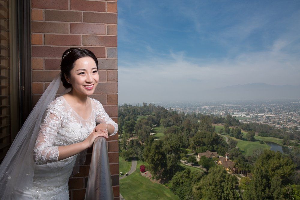 A bride in a wedding dress is standing on a balcony overlooking a city.
