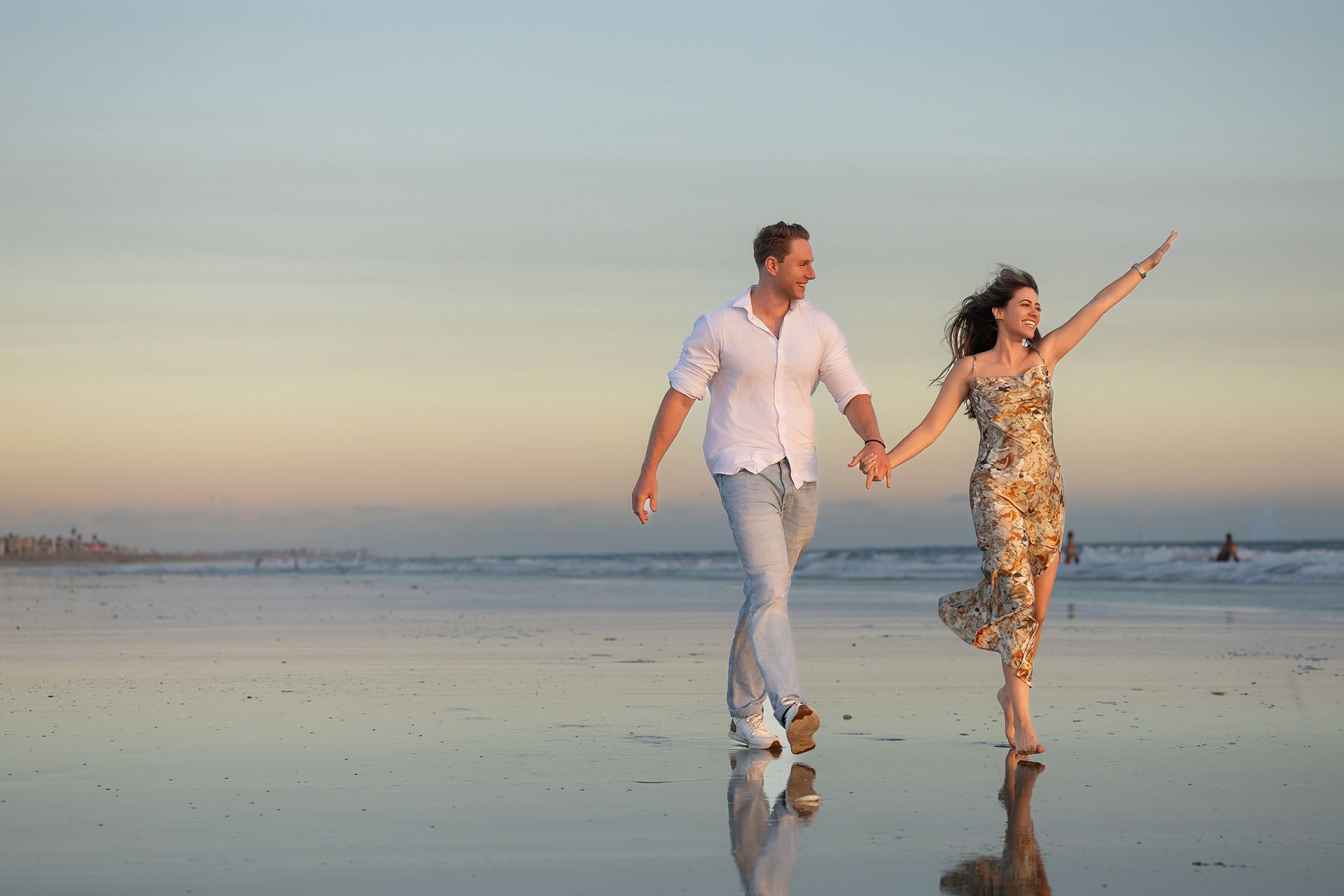 A man and a woman are walking on the beach holding hands.
