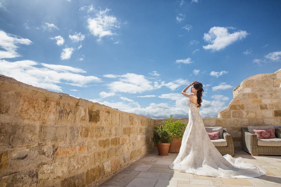A woman in a wedding dress is standing on a balcony looking at the sky.