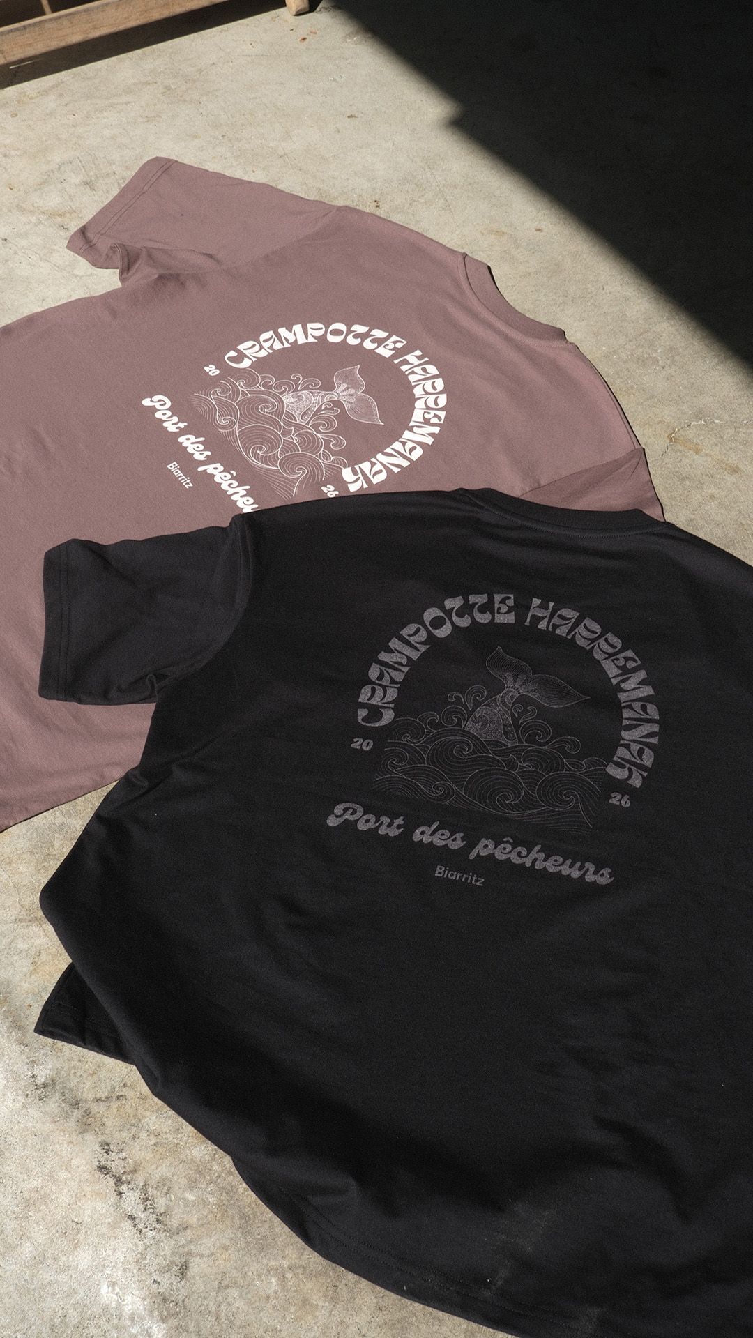 Deux t-shirts, l'un mauve et l'autre noir, posés à plat sur un fond clair, tous deux ornés de motifs graphiques blancs identiques.