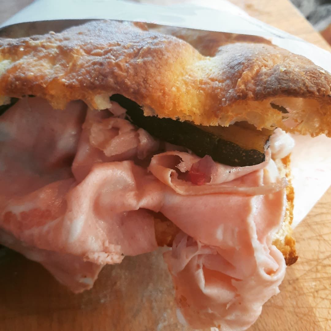 Primo piano di un panino con mortadella tagliata a fette sottili e un ingrediente scuro all'interno, servito su pane spesso e dorato.
