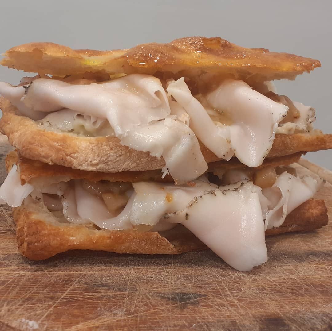 Un sandwich a due strati, composto da croccanti strati di pane dorato farciti con sottili fette di carne bianca, servito su una piastra di legno.