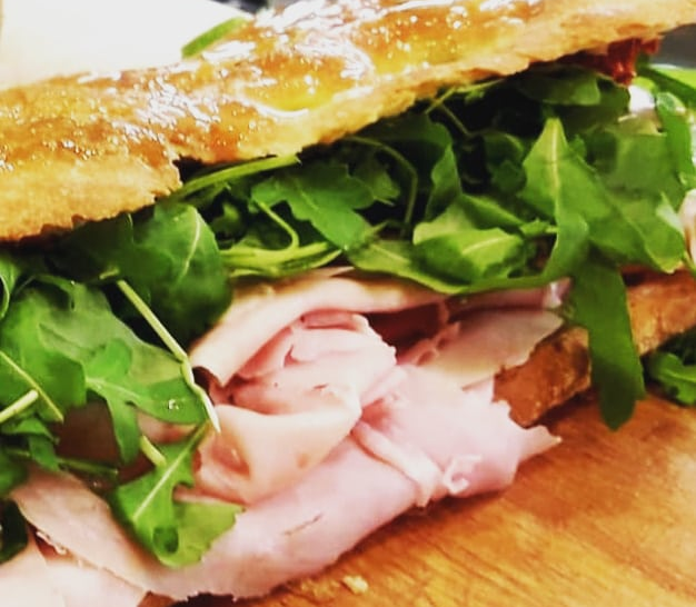 Un panino su una superficie di legno con strati di prosciutto cotto a fette e una generosa porzione di rucola fresca.