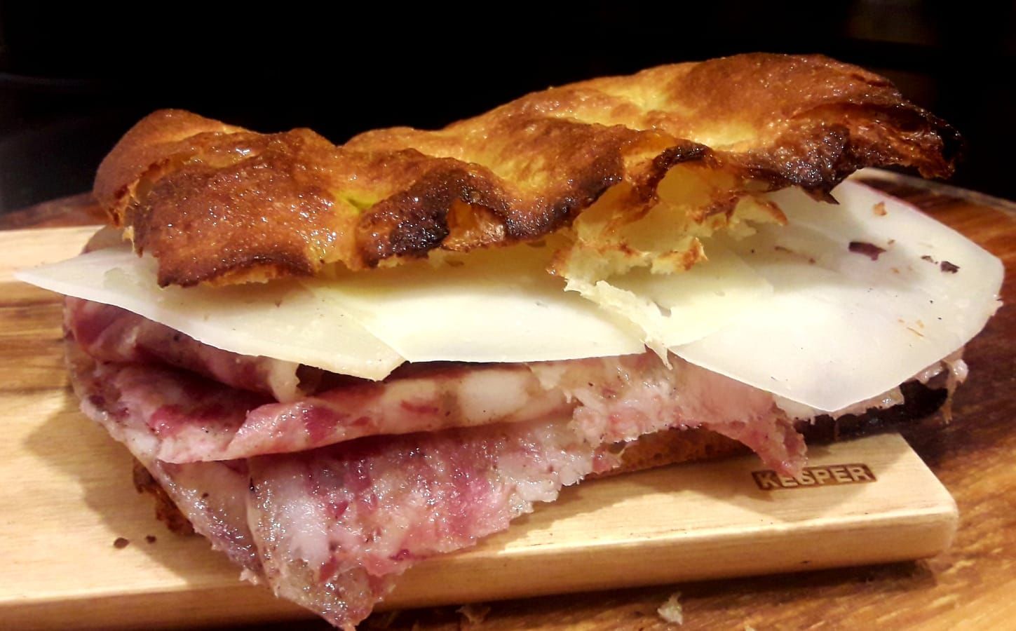 Primo piano di un panino con salumi e formaggio tagliato a fettine sottili su un tagliere di legno.