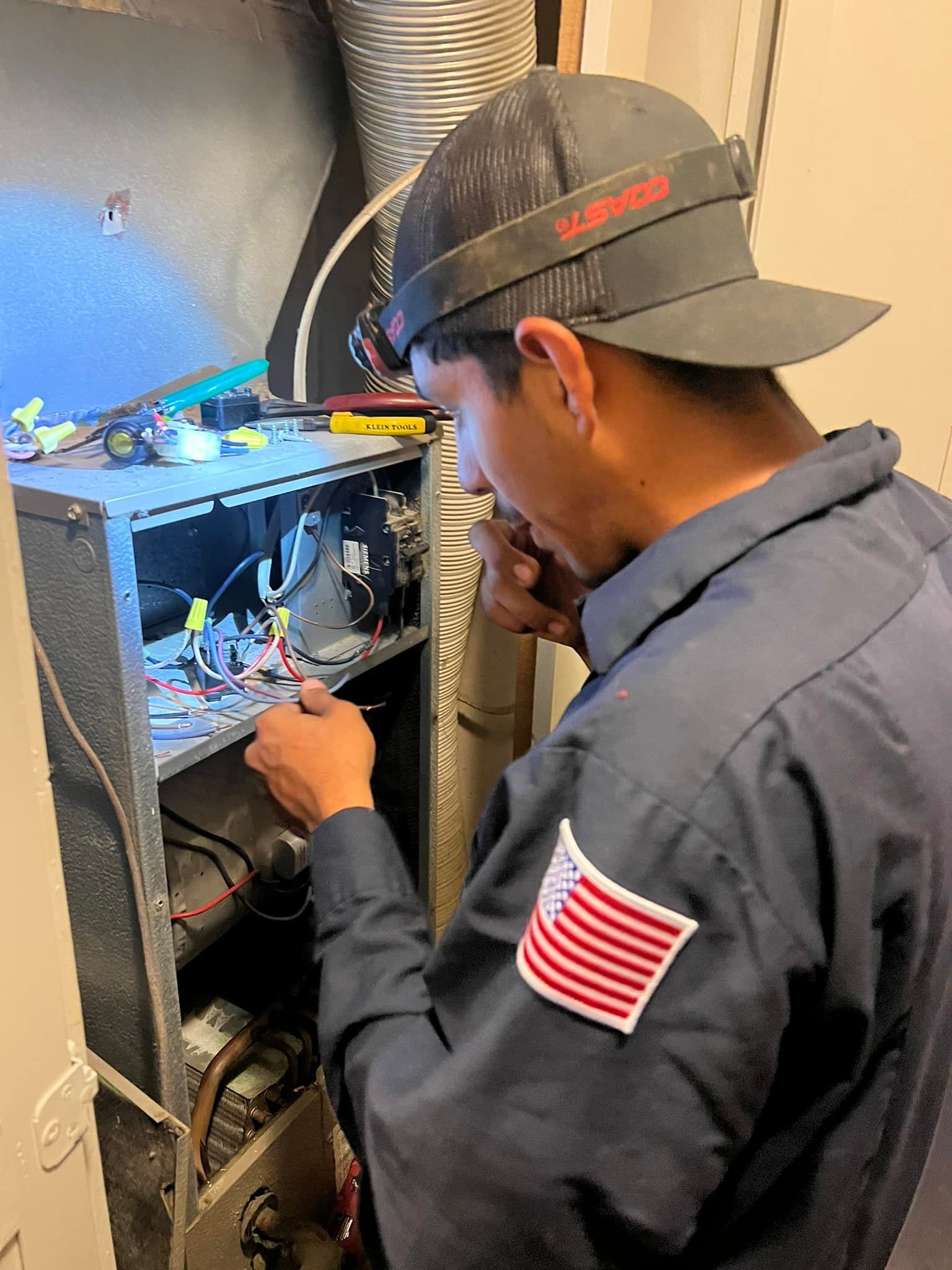 HVAC technician fixing a furnace, wearing a cap with a light, in a utility room.