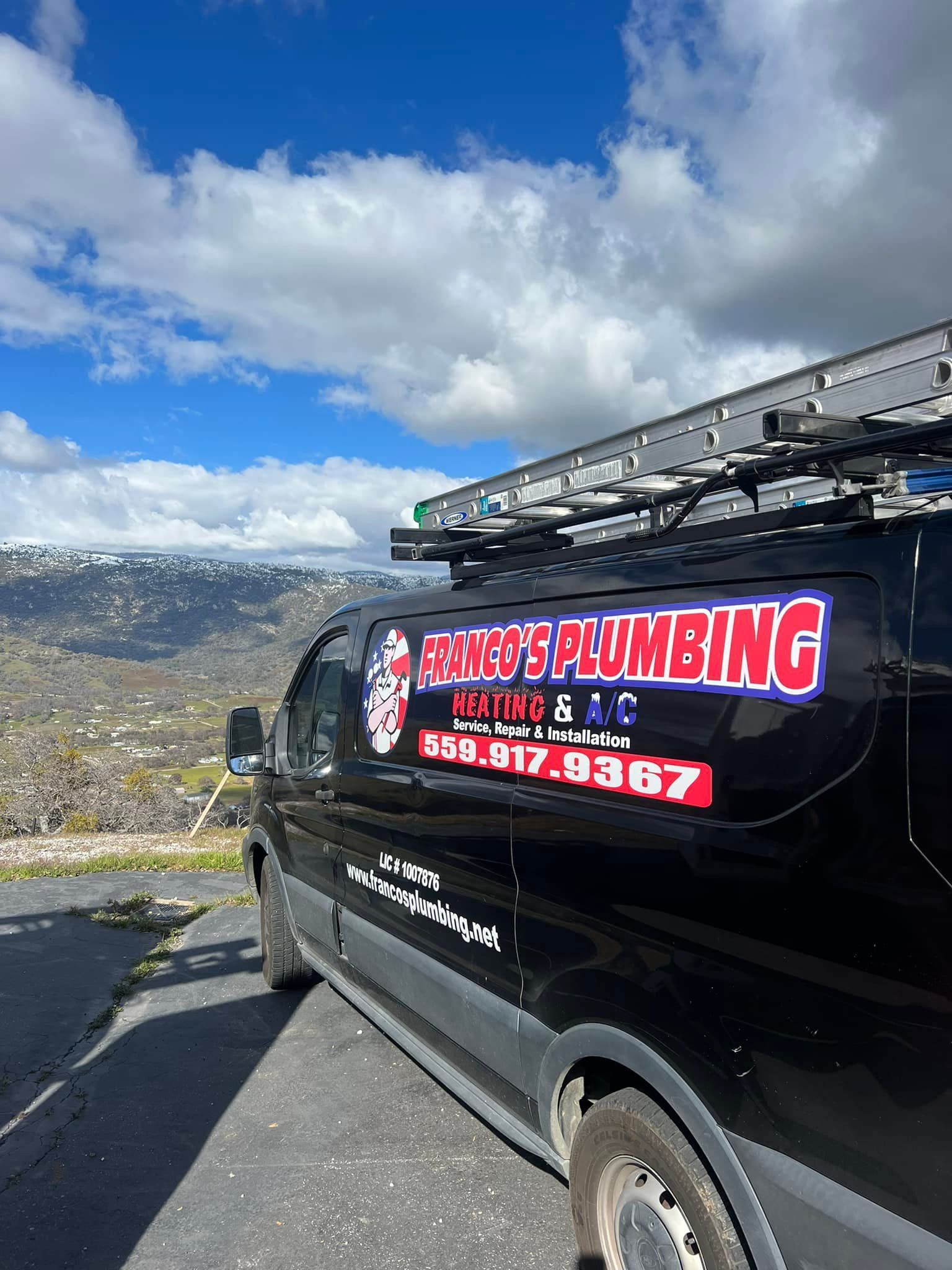Black plumbing van with ladder on roof, parked overlooking a hilly landscape under a cloudy sky.