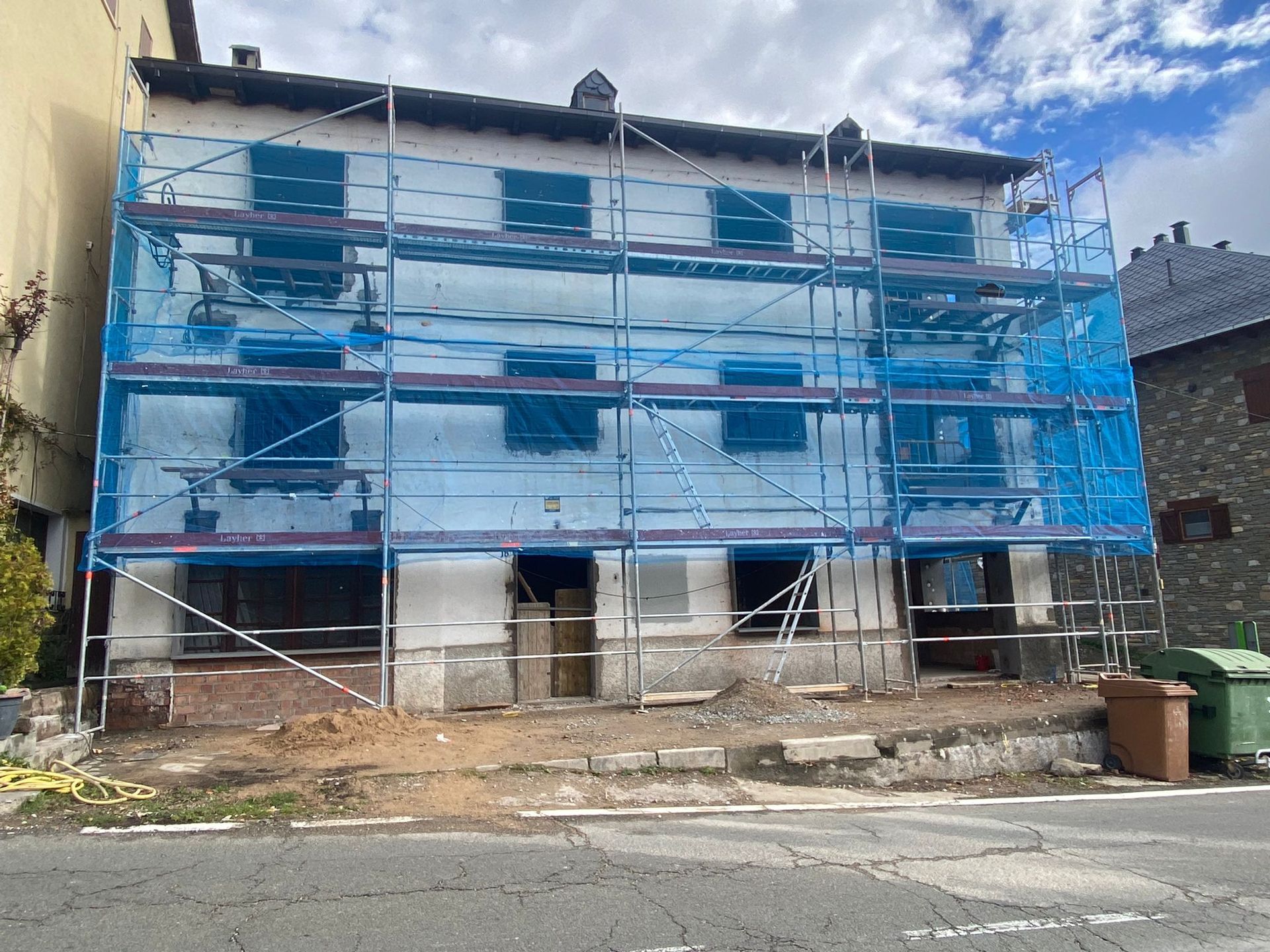 Edifici en reforma amb bastides i xarxa de seguretat blava; vista exterior.