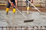 Treballadors de la construcció allisant formigó humit amb eines en una obra.