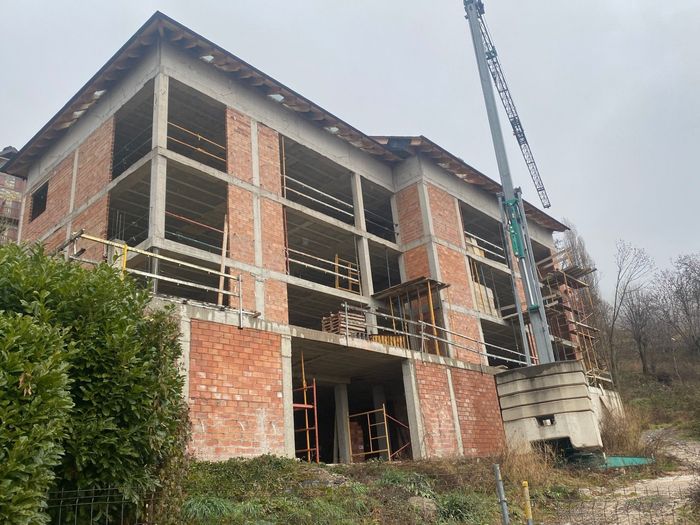 Edifici en construcció amb grua, maó vermell i estructura de formigó.