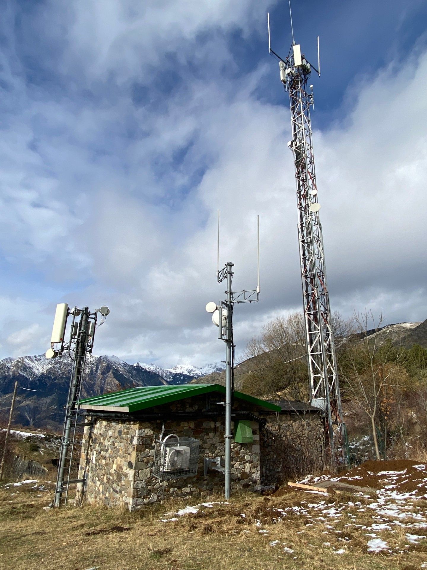 Torres de ràdio i petit edifici de pedra en un paisatge muntanyós, sota un cel ennuvolat.