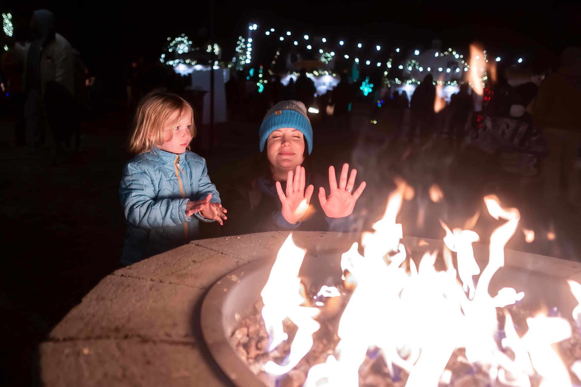 A Parent And Child Warming Up By A Fire On A Chilly Night, The Fire Pit Is Made Out Of Curved Cinder Blocks